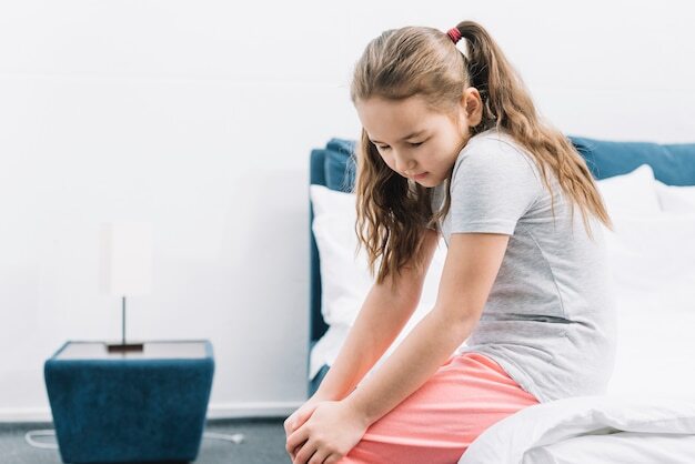 Close-up of a girl sitting on bed suffering from knee pain